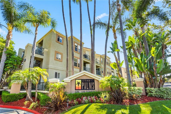 Front view of a multi-story apartment building with balconies and a sign reading 'The Palms'.