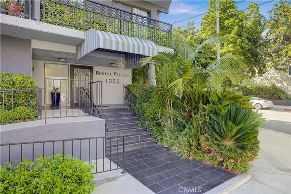 Front view of a residential building entrance with stairs and plants.