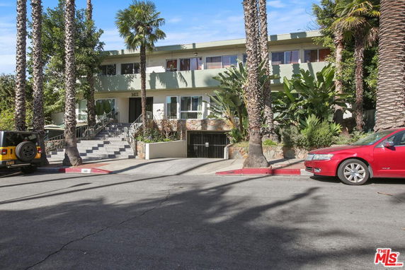 Front view of a two-story building with steps leading to the entrance and surrounding palm trees.