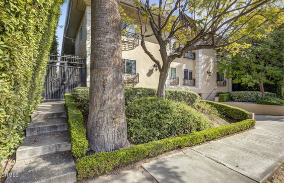 Front view of a two-story house with decorative balconies and surrounding greenery.