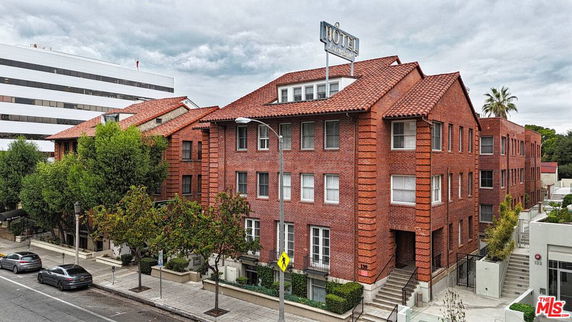 Front view of a red brick multi-story building with a sign on the roof.