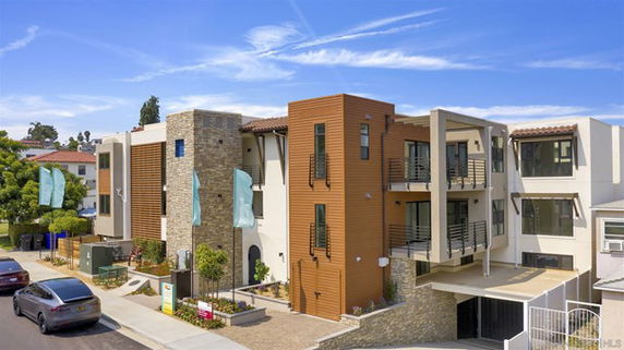 Front view of a modern multi-story apartment building with balconies and a stone facade.