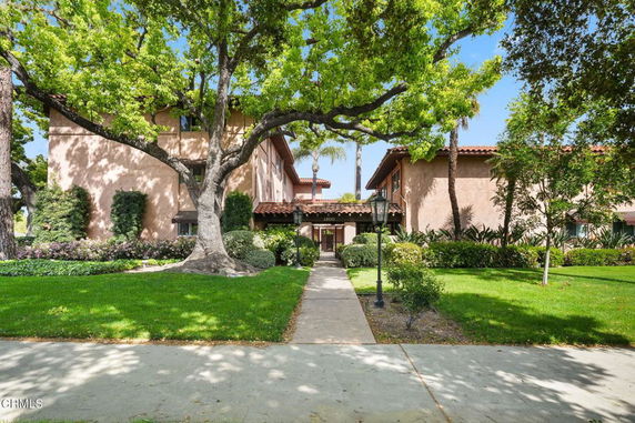 Front view of a two-story house with a tiled roof and lush greenery.