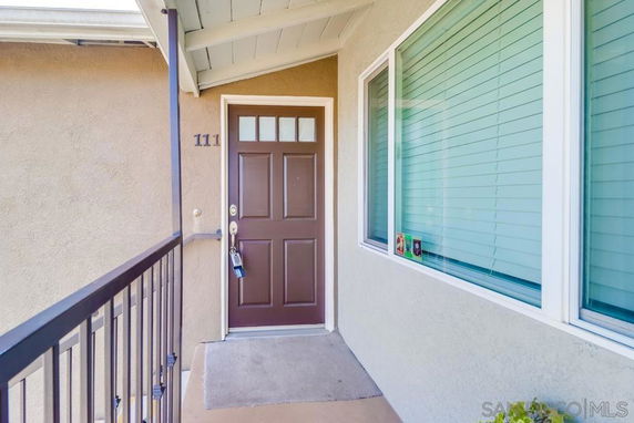 Front view of an apartment entrance with a brown door and a railing on the left.