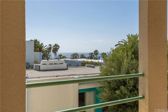 View from a building balcony showcasing rooftops, palm trees, and the ocean in the distance.