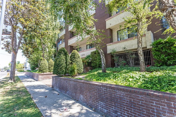 Front view of a multi-story brick apartment building with landscaped greenery.