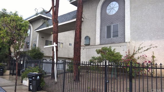 Front view of a multi-story building with arched windows and a fenced yard.