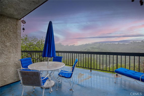 Balcony with outdoor seating offering a scenic view of hills and sky.