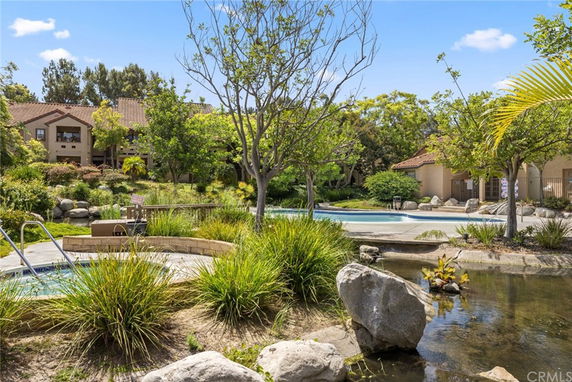 Outdoor swimming pool area with surrounding greenery and buildings.