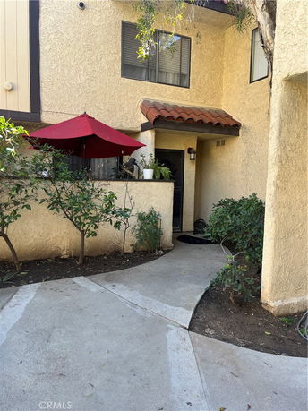 Front view of a two-story house with a red umbrella and small garden area.