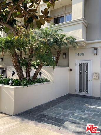 Front view of a building entrance with plants and a decorative door.