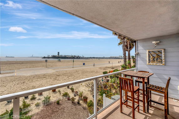 View from a balcony overlooking a beach with a table and chairs on the balcony.