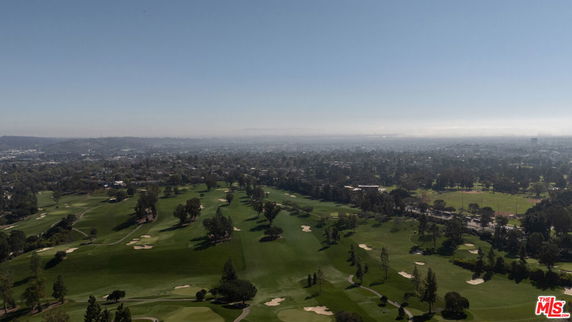 Wide-angle view of a landscape with green fields and trees, extending towards a distant cityscape under a clear sky.