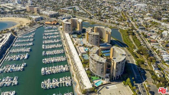 Aerial view of a large building complex with circular and rectangular structures, located near a marina with numerous boats.