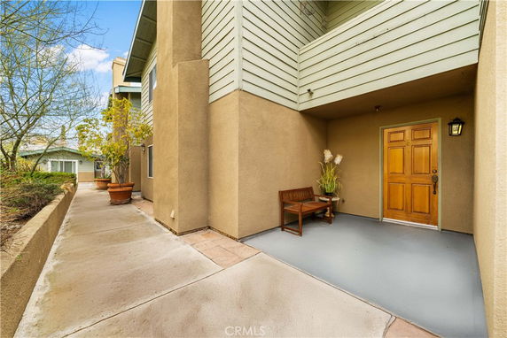 Entrance view of a residential building with a wooden door and small porch seating.
