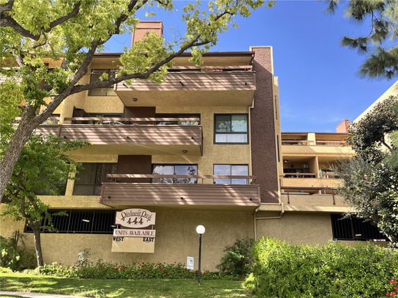 Front view of a multi-story residential building with balconies and a sign indicating available units.