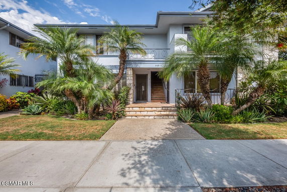 Front view of a two-story house with a garden and palm trees.