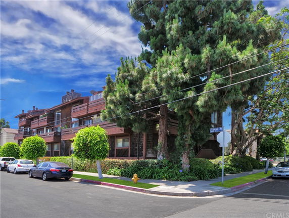 Front view of a multi-story residential building with balconies and surrounding trees.