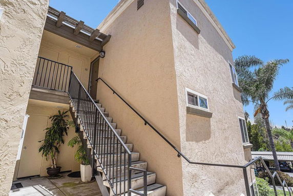 Front view of a multi-story building with exterior staircase and beige stucco walls.
