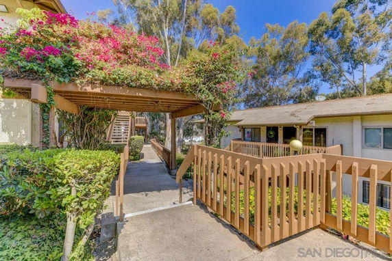 Front view of a residential building with wooden railings and an arched pergola covered in flowering plants.