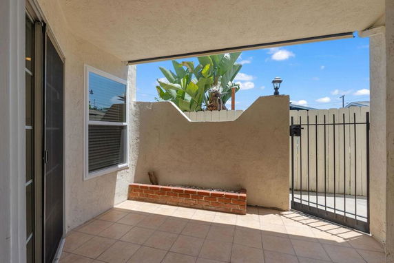 Outdoor patio area with tile flooring, partial wall, and gate.