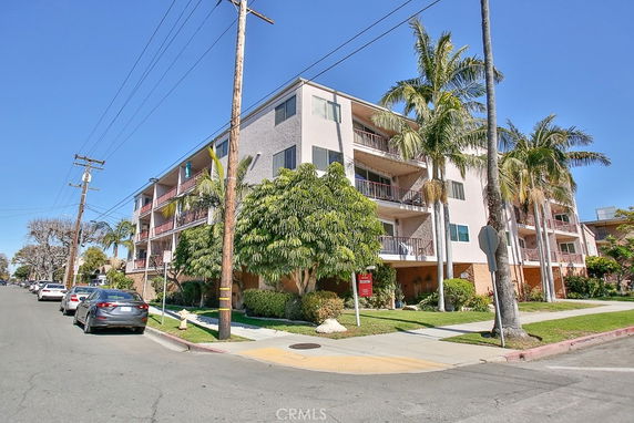 Front view of a multi-story apartment building with balconies and palm trees.