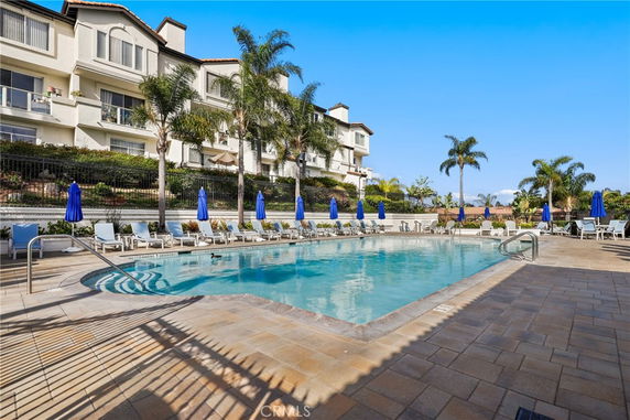 Outdoor swimming pool area with lounge chairs and umbrellas in front of a multi-story building.