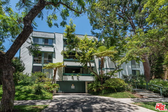 Front view of a multi-story building with trees and shrubbery around it.