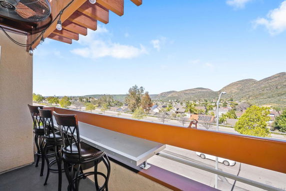 Panoramic view of surrounding residential area and hills from a balcony with chairs.