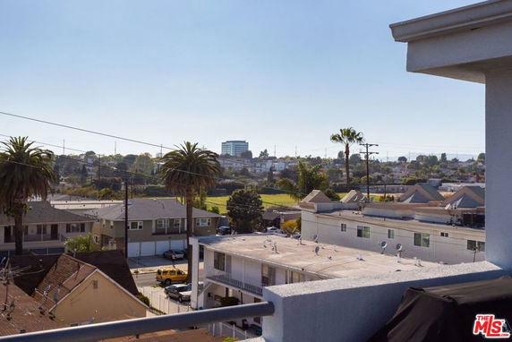 Panoramic view from a building showing rooftops and a cityscape with palm trees and distant hills.