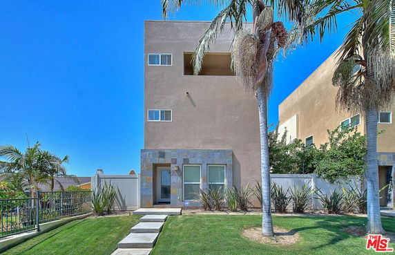 Front view of a contemporary multi-story building with palm trees and a well-maintained lawn.