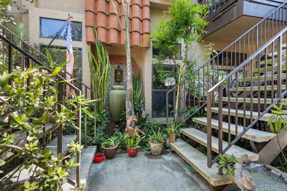 Front view of a multi-story building entrance with stairs and plants.
