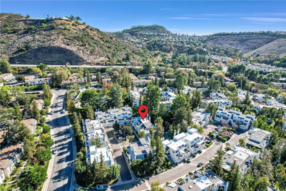 Aerial view of a residential area with multiple buildings, trees, and hills in the background.
