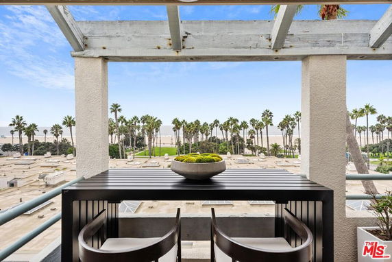 Panoramic view of a beach and palm trees seen from a balcony with outdoor seating.