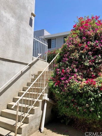 Staircase leading to an upper level of a building with floral bush on the side.