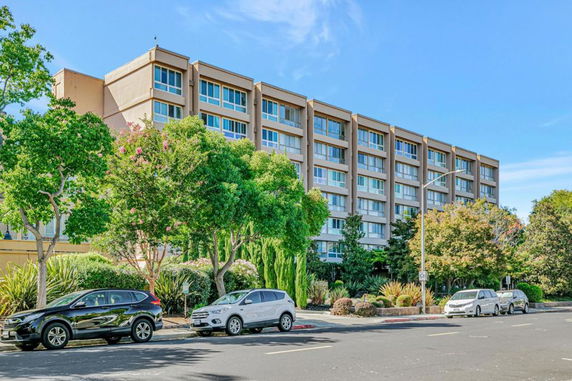 Front view of a multi-story building with large windows and trees in front.