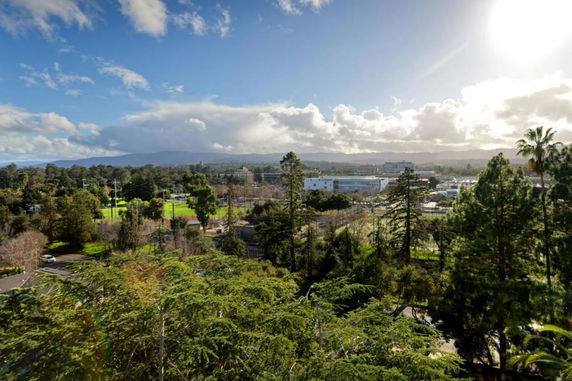 Panoramic view of a landscape with trees, buildings, and mountains in the background.