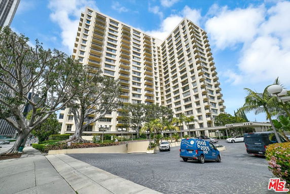 Front view of a large multi-story residential building with surrounding trees and parked cars.
