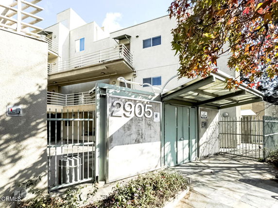 Front view of a modern multi-story building with metal railings and gated entrance.