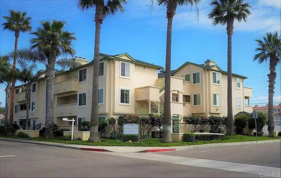 Front view of a multi-story residential building with balconies and surrounded by palm trees.