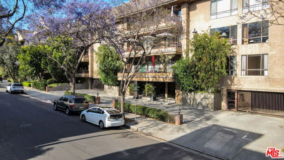 Front view of a multi-story residential building with large windows and a parking area in front.