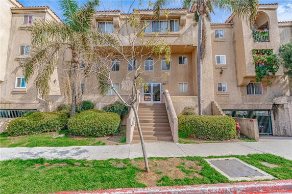 Front view of a multi-story residential building with entry stairs and palm trees.