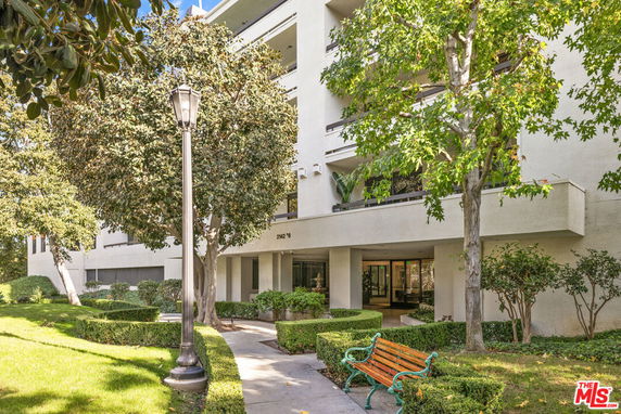 Front view of a multi-story residential building with balconies and a landscaped entrance.