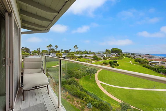 View of a landscaped area with paths, trees, and a distant ocean from a balcony.
