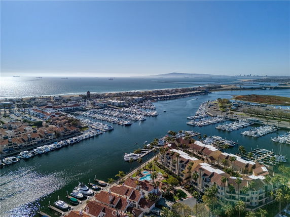 Wide angle view of a marina with numerous boats docked, surrounded by residential buildings and the open sea in the background.