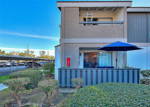 Front view of a two-story building with a balcony and patio, including a blue umbrella.