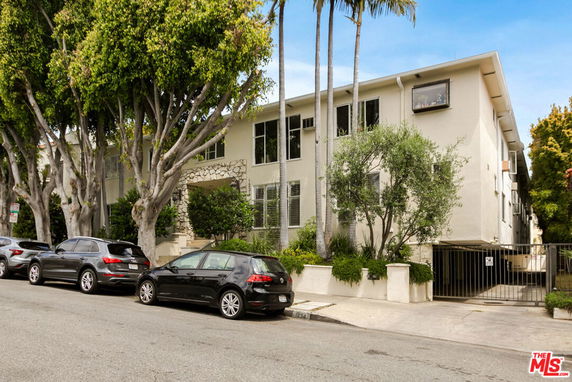 Front view of a two-story apartment building with trees and parked cars.
