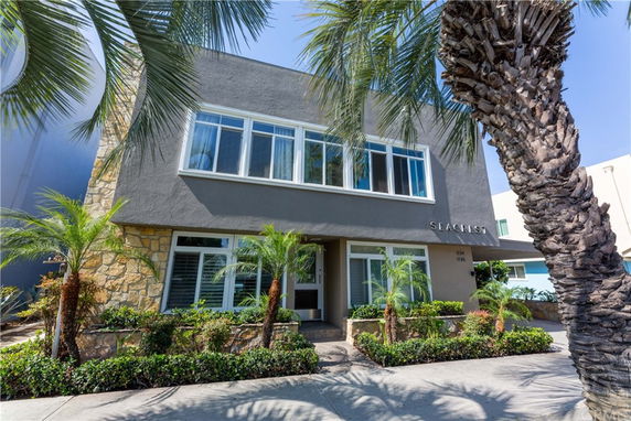 Front view of a two-story building with a mix of stone and gray exterior, large windows, and palm trees in the landscaping.