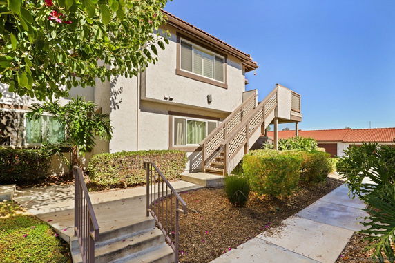 Front view of a two-story residential building with external staircase and landscaped walkway.