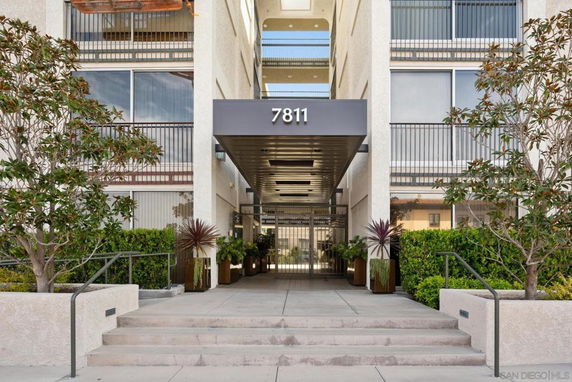 Front view of a multi-story building entrance with stairs and greenery.
